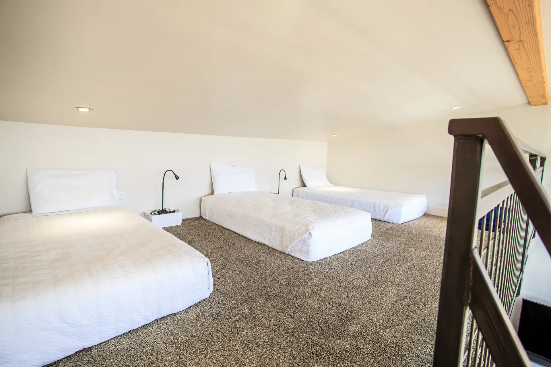 A loft space featuring three single beds with white bedding arranged on a beige, textured carpet under a sloped ceiling.