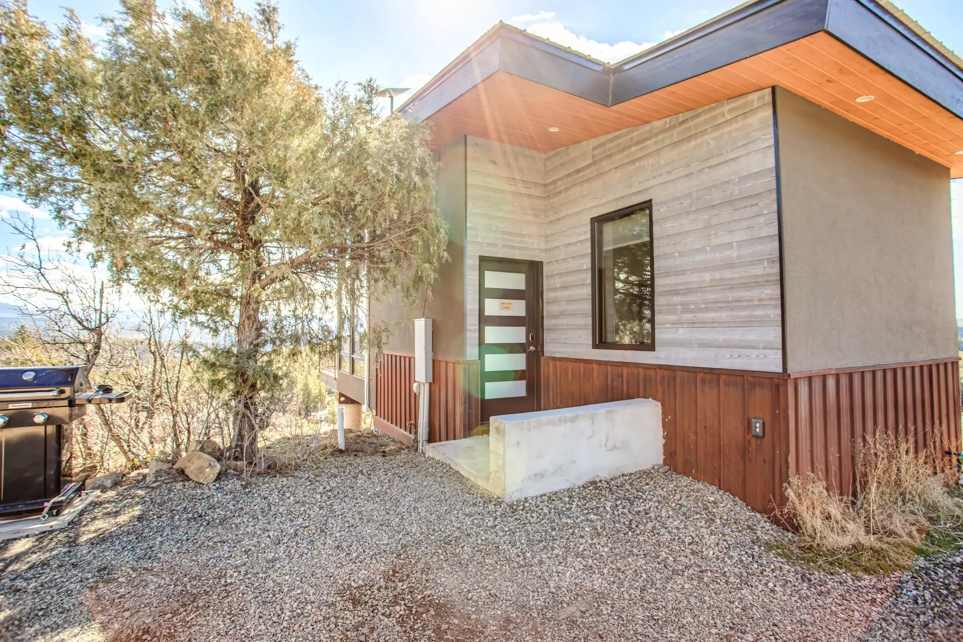 A modern home exterior with horizontal wood siding, a flat roof, a glass-paneled door, and a low stone wall on gravel.