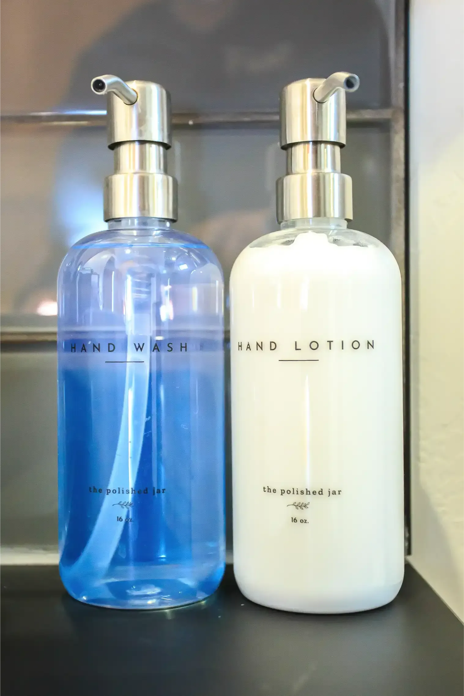 Two pump-top bottles sit on a counter: one with blue hand soap and one with white hand lotion.