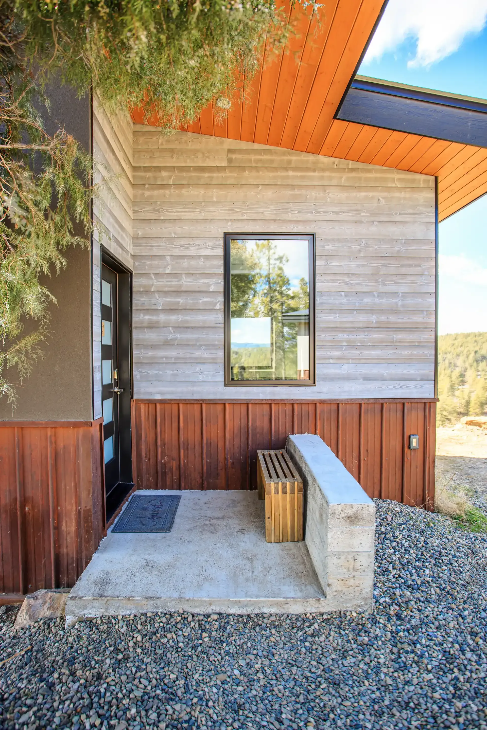 A modern home exterior with horizontal wood siding, a vertical wood base, a single-pane window, and a concrete entrance.