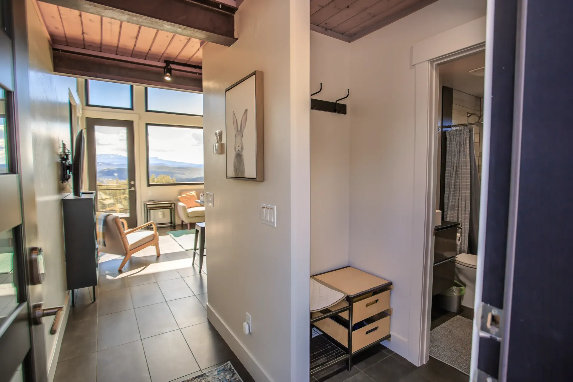 A brightly lit entryway with a mudroom area featuring coat hooks and storage, leading to a living room with mountain views.