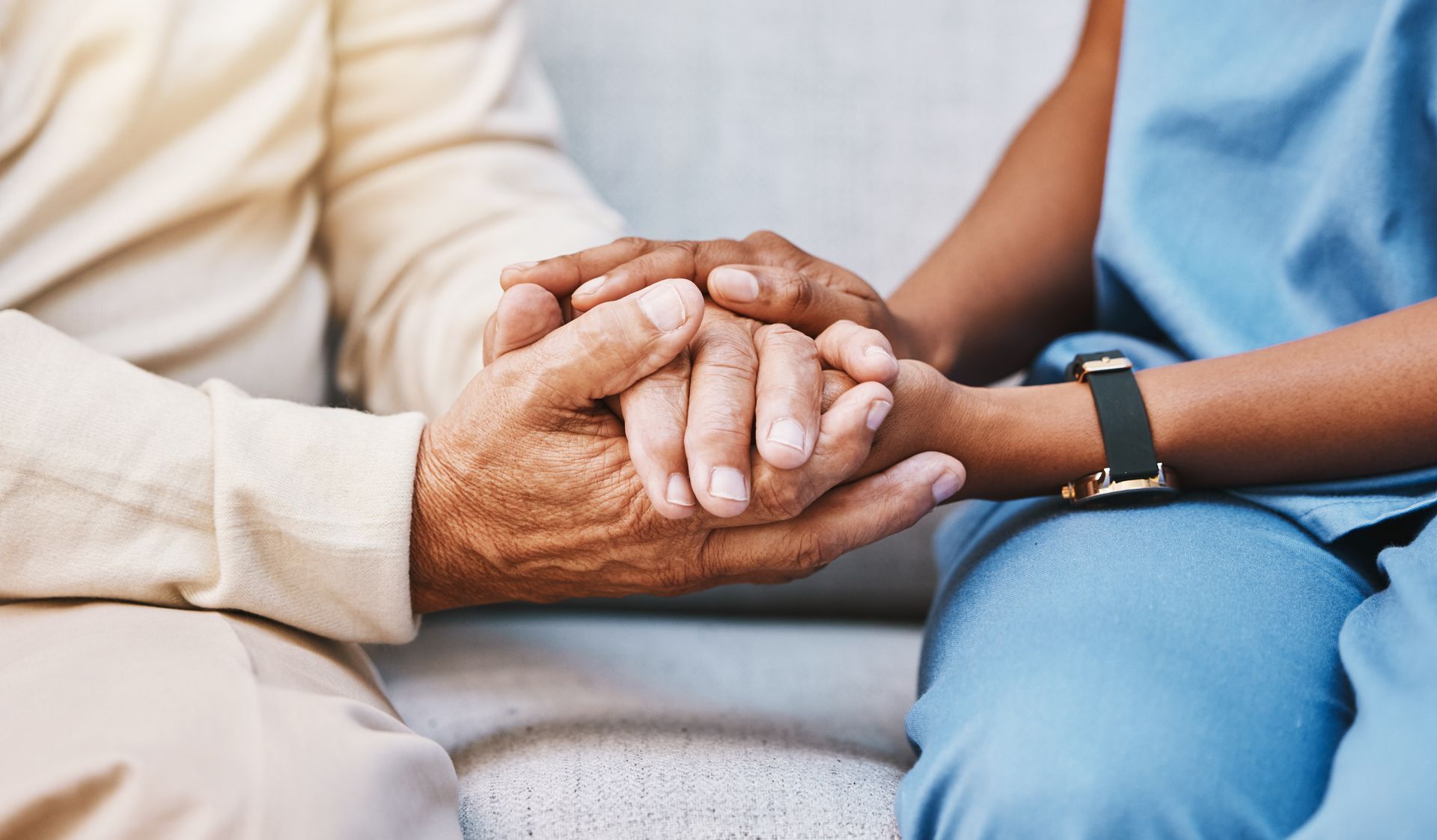 Two people holding hands in a supportive gesture, one wearing a smartwatch on a couch