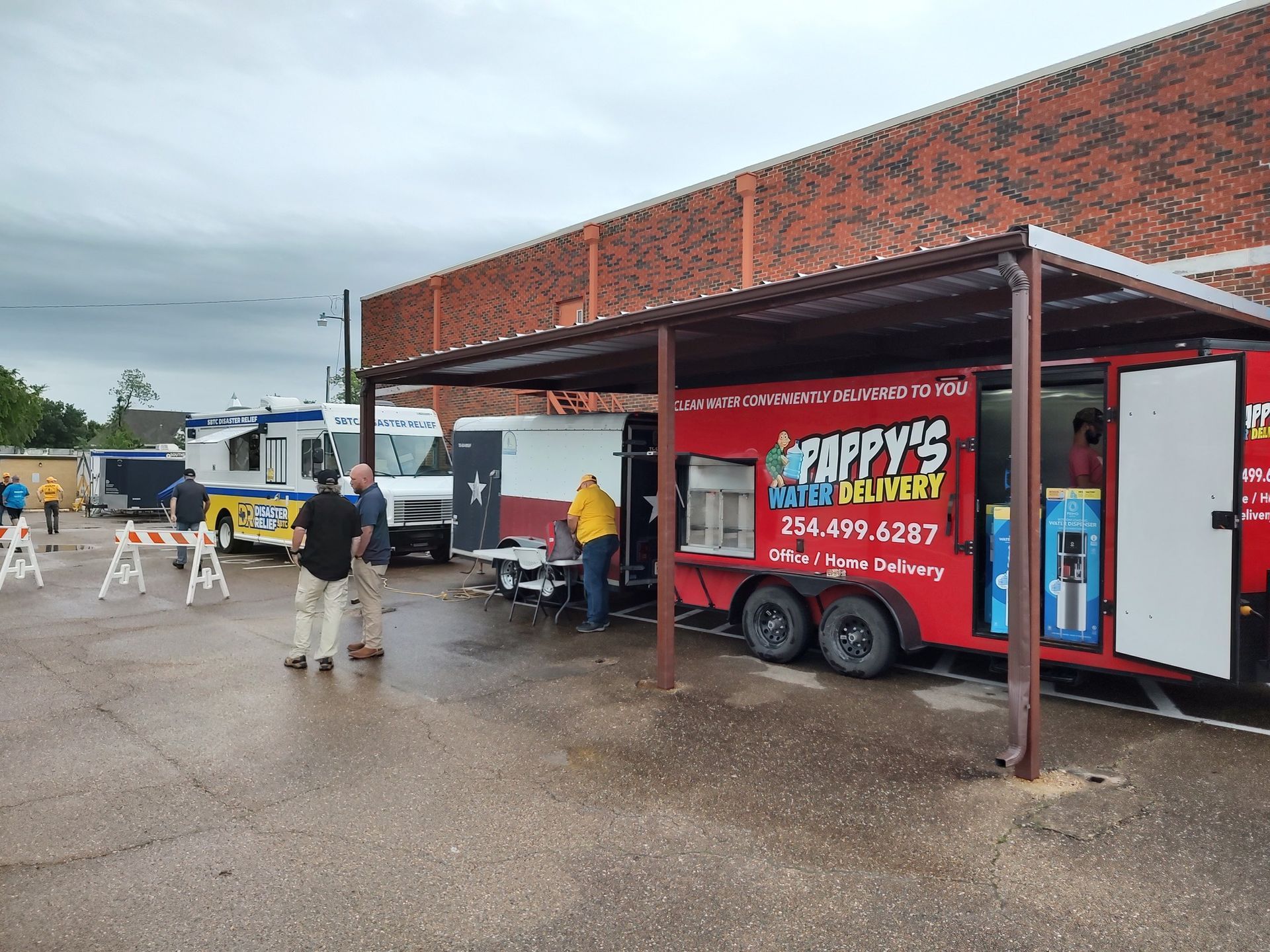 Food trucks parked under a canopy. People wait in line. A red trailer has
