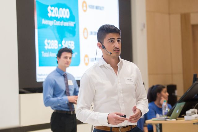 A man wearing a headset is giving a presentation in front of a large screen.