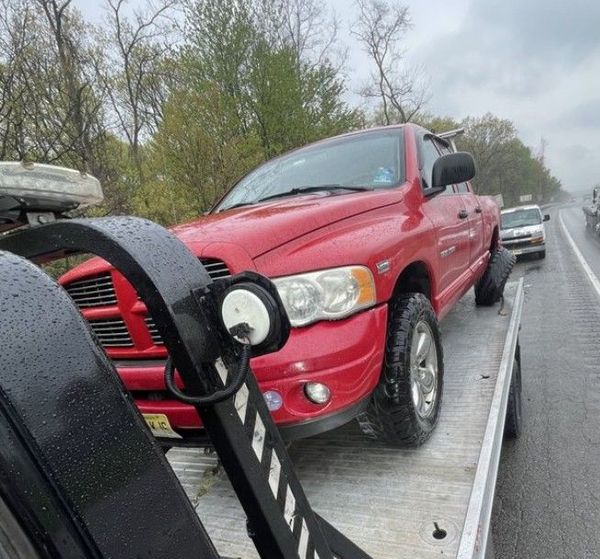 A red car is being towed down a highway by a tow truck.