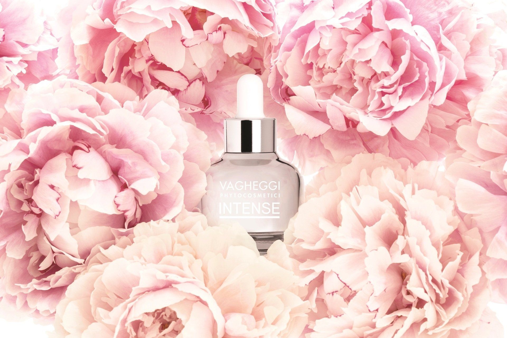 Eine Flasche Serum ist von rosa Blumen umgeben.