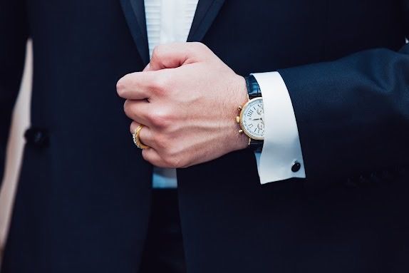 Man's hand in a black suit adjusting his jacket, showing a gold watch on his wrist.