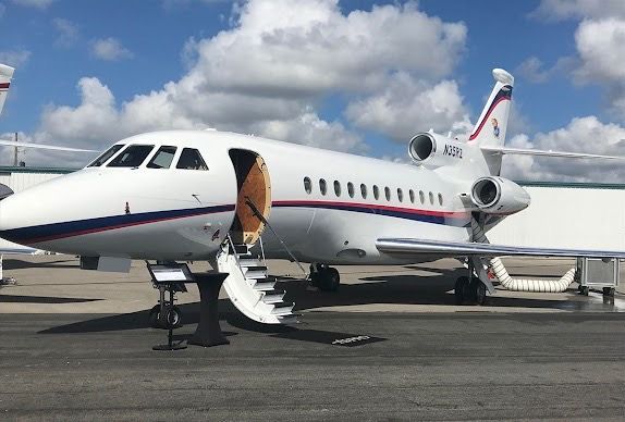 White private jet with open door on tarmac under blue sky.