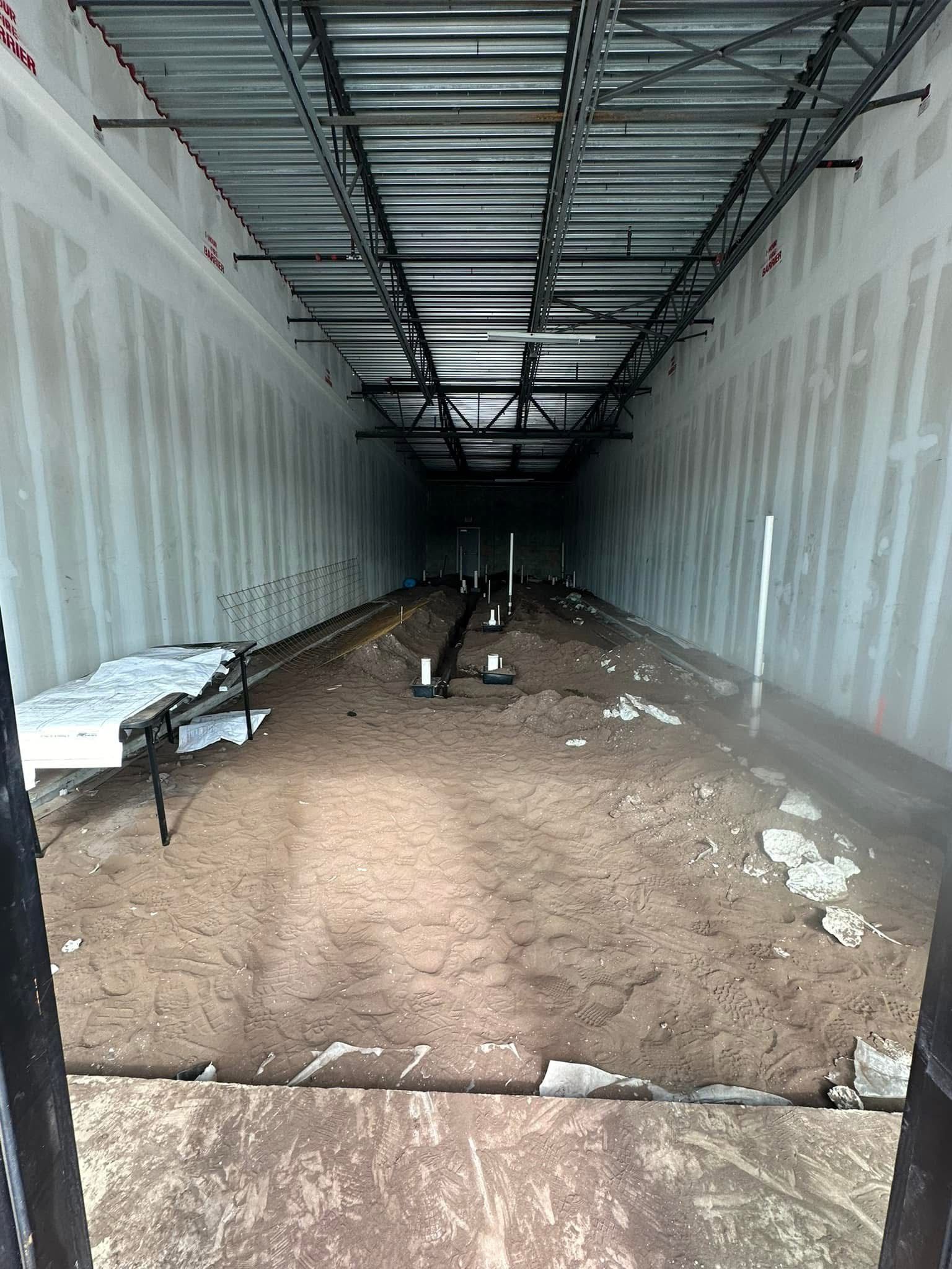 Construction of an interior space. Walls and ceiling framed, dirt floor extends into the darkness.