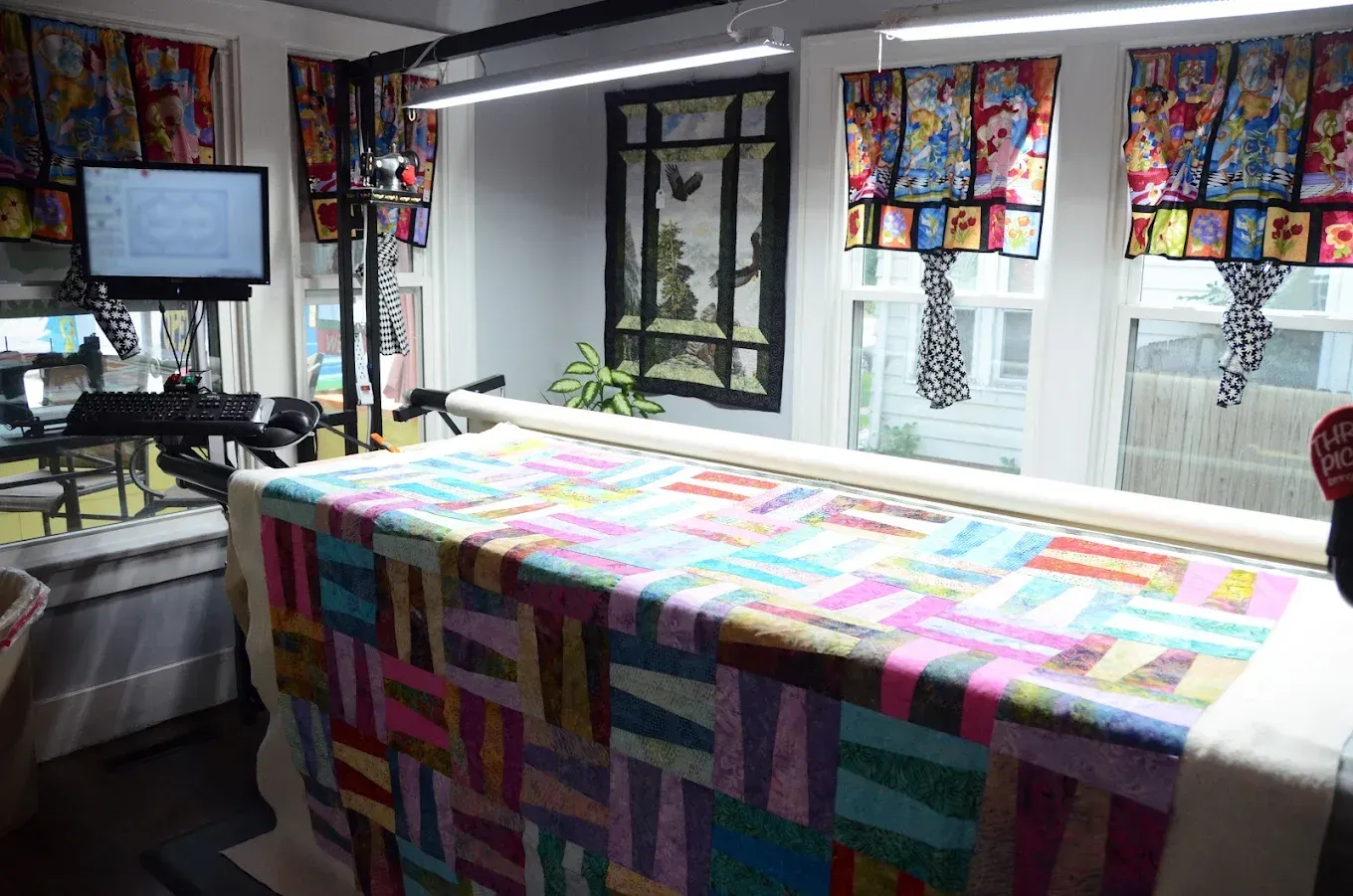 Colorful quilt covering a table in a bright studio with sewing materials and windows in the background