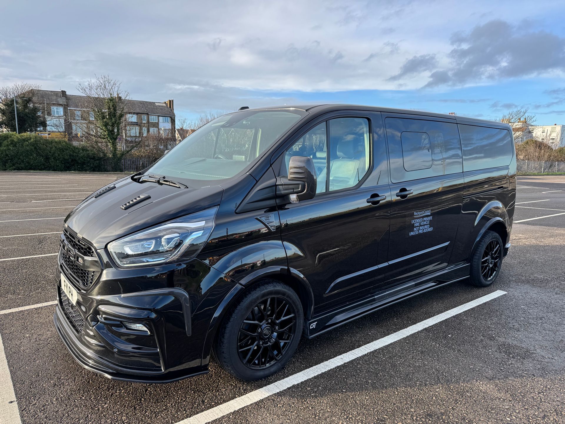 Black custom van parked on an asphalt lot under a cloudy sky.