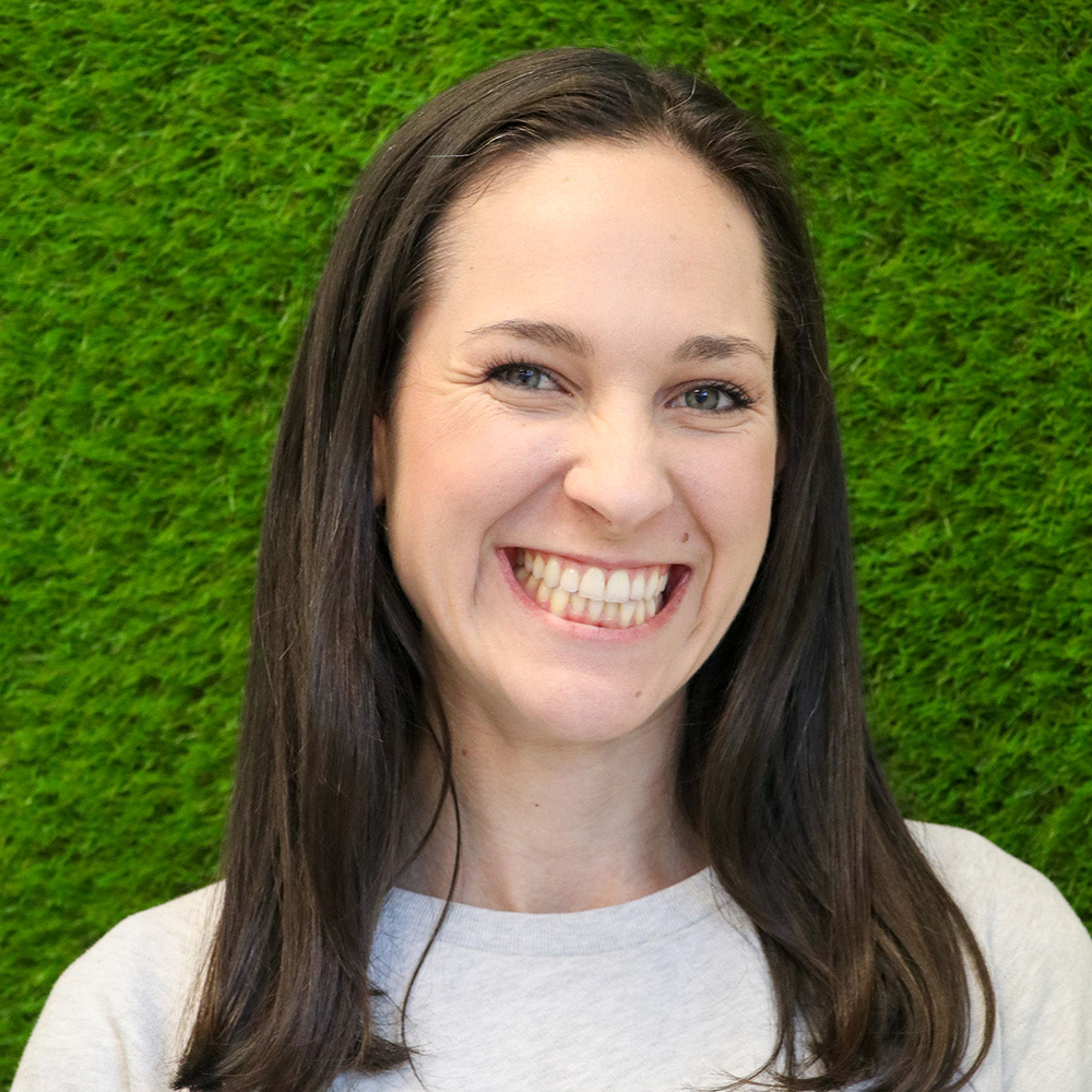 A woman is smiling in front of a green wall.