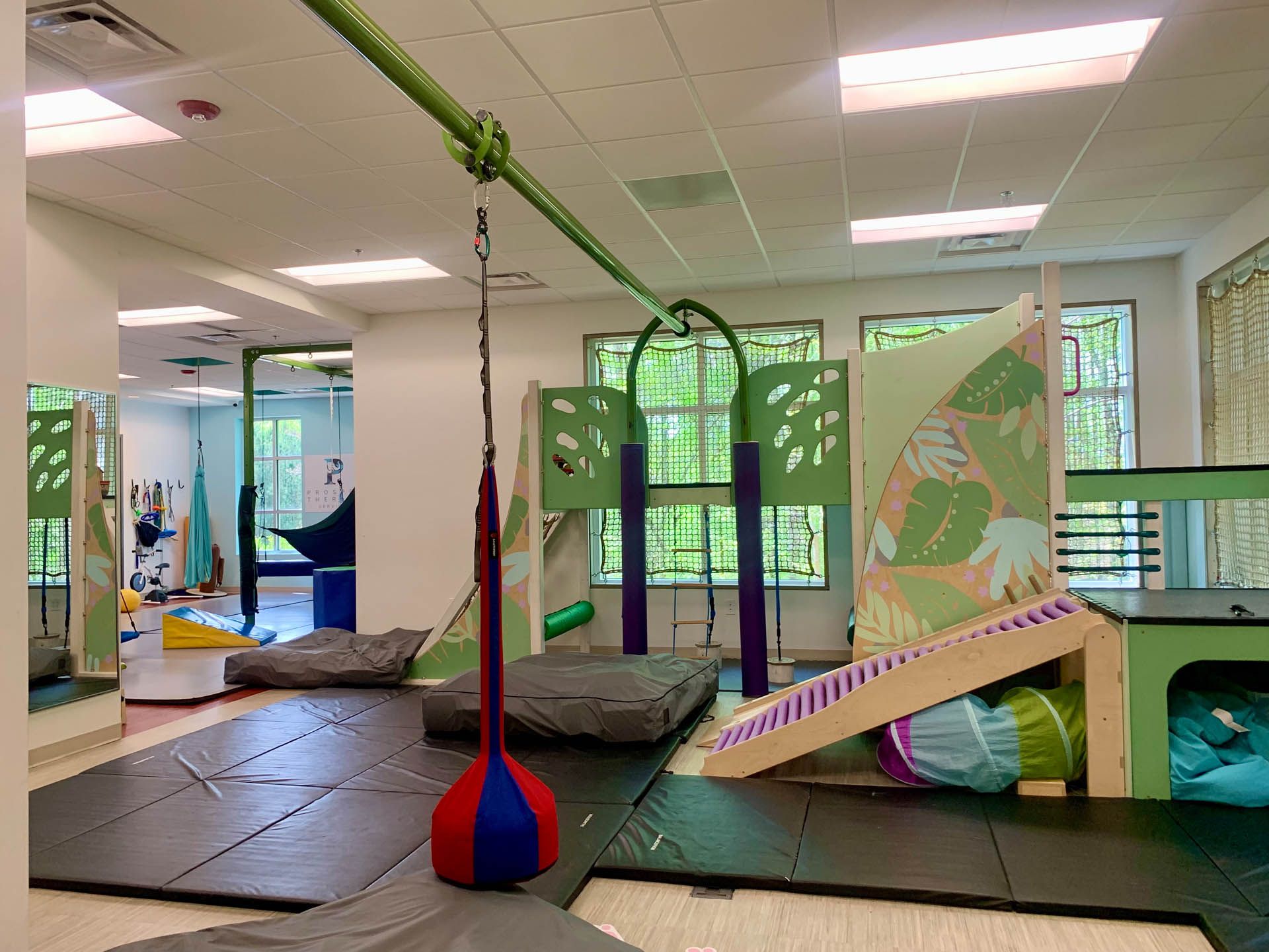 An accessible indoor play area with climbing structures, swings, and mats.