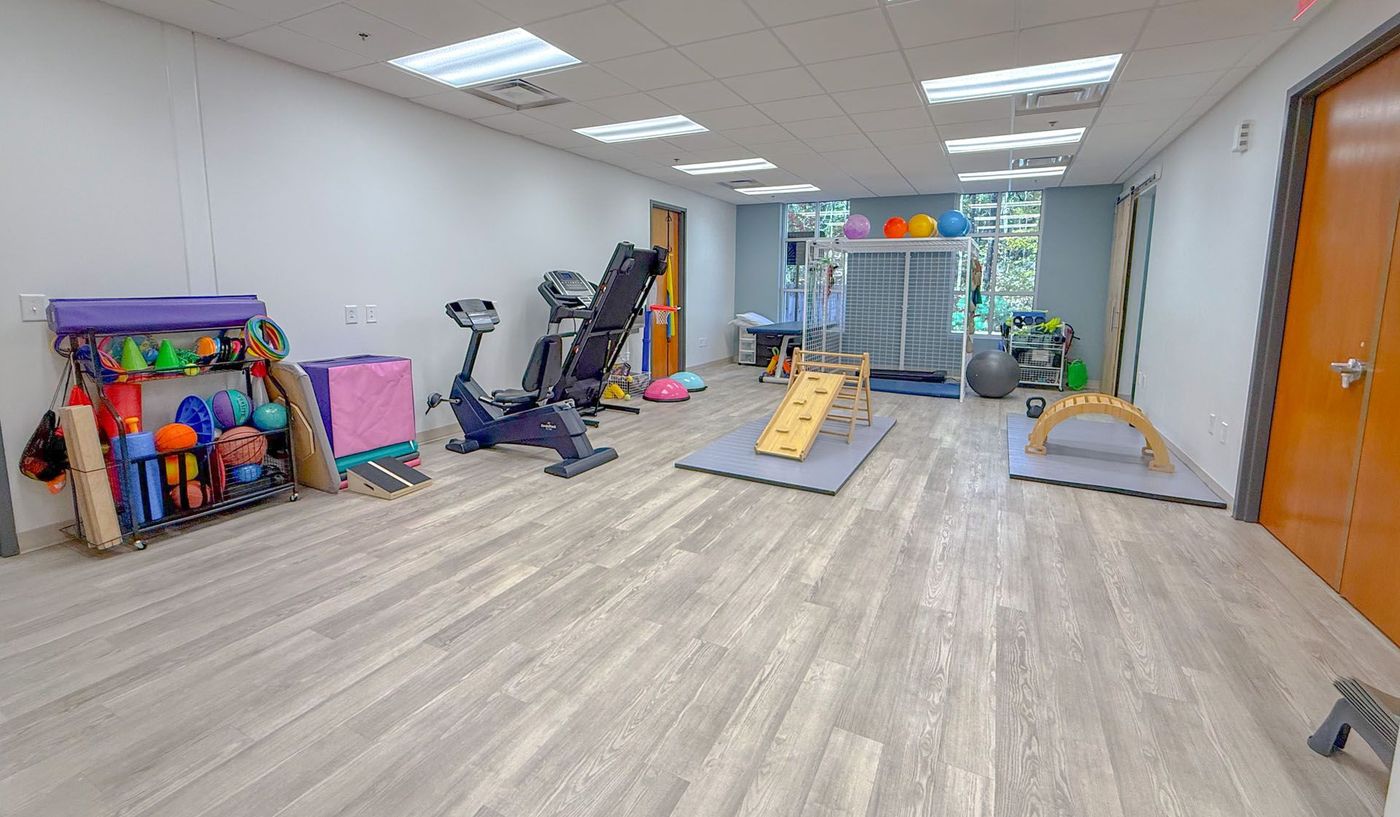 Therapy room with exercise equipment, including weights, bikes, balance boards, and stairs.