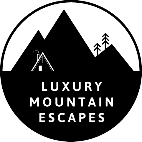 Black circular logo with mountains, cabin, trees, and the words “Luxury Mountain Escapes”