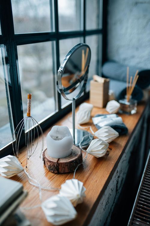 Window-side wooden table with a mirror, candles, and folded white paper decorations