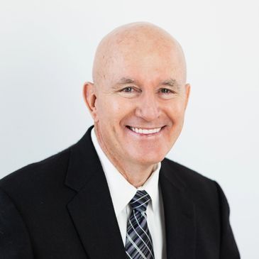 Bald man in black suit smiling, headshot against a white background.