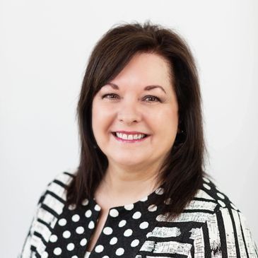Woman with dark hair and a patterned jacket smiling at the camera.