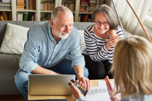 Older couple consults with a financial advisor, looking at documents and a laptop in a home setting.