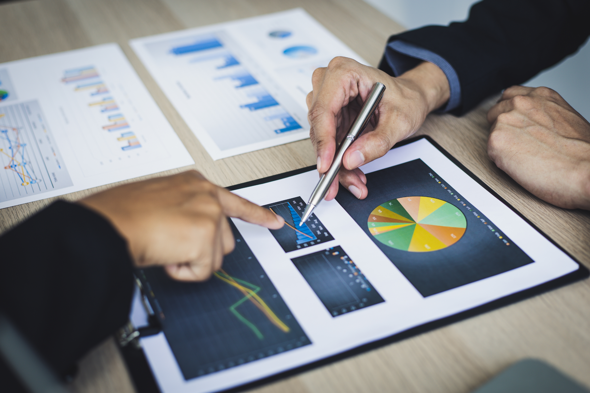 Two people in suits reviewing financial reports with charts and graphs at a desk.