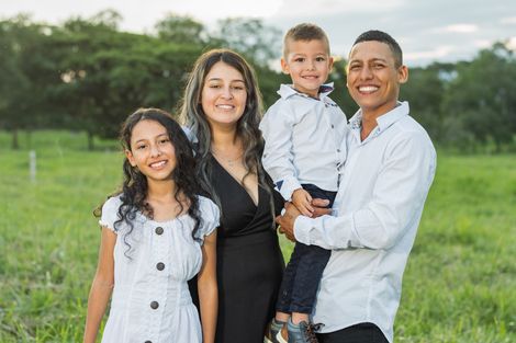 Family of four smiles at the camera in a grassy field.