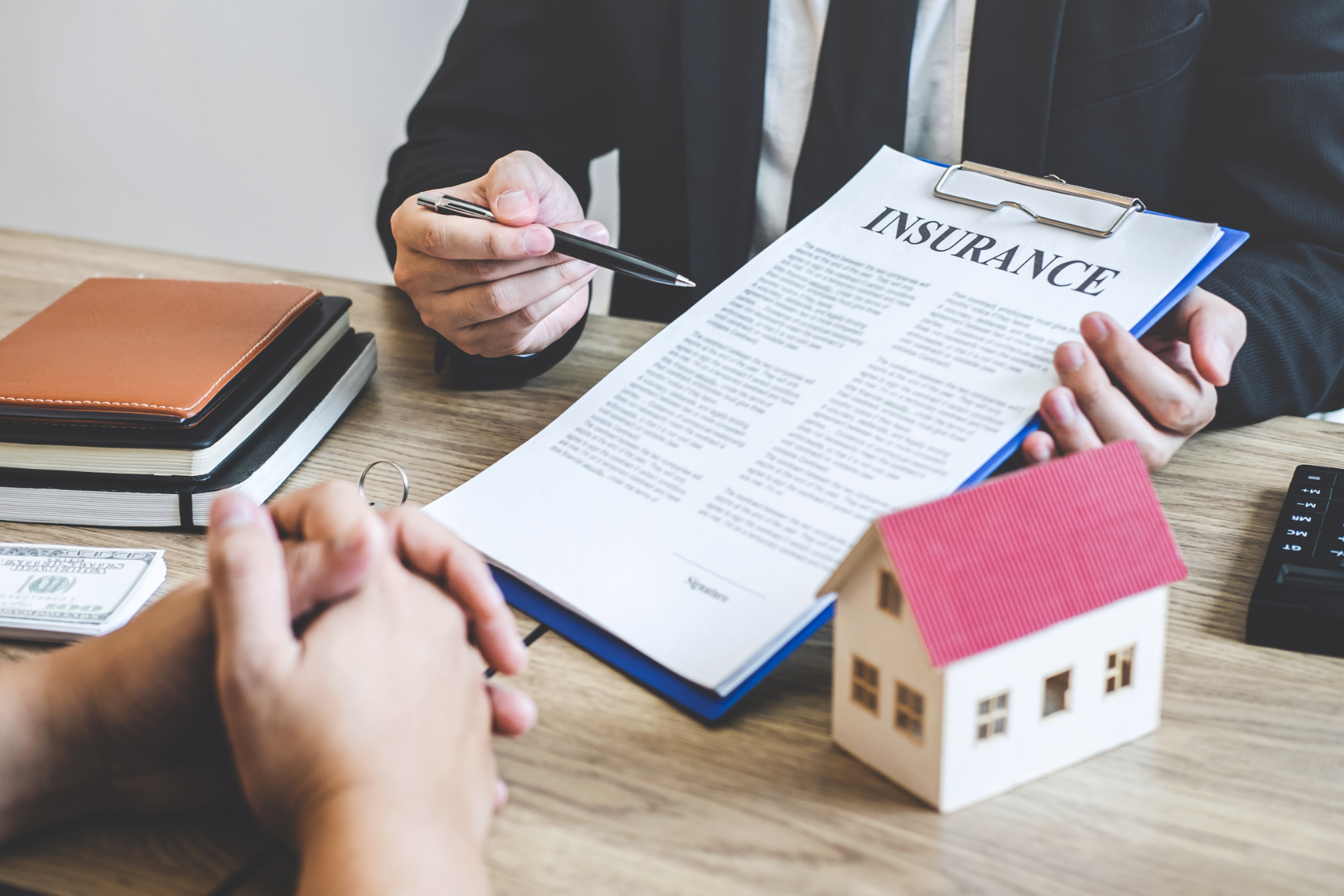 Person in suit pointing at insurance document, with house model and client.