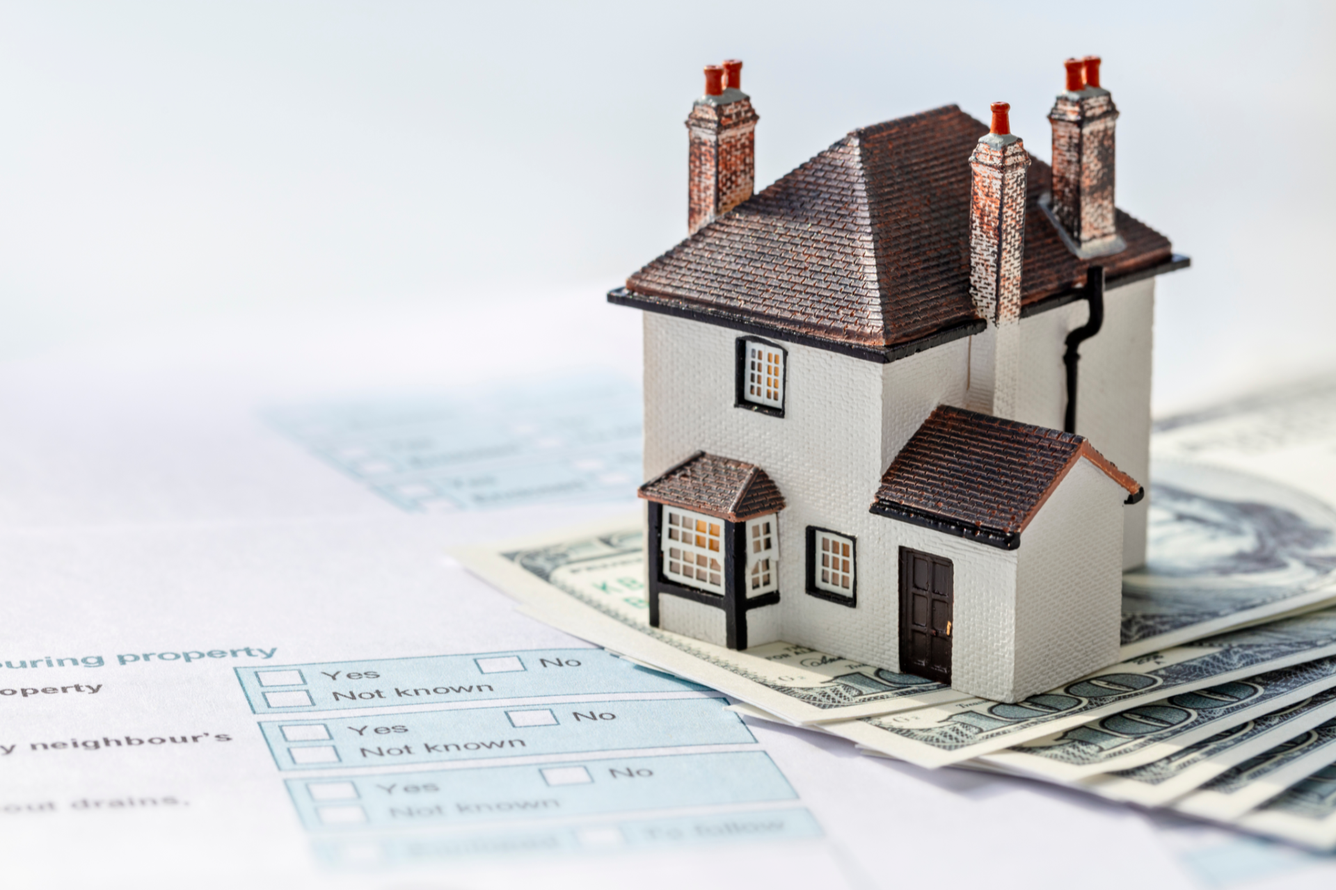 Miniature house on a stack of money, with a real estate form in the background.