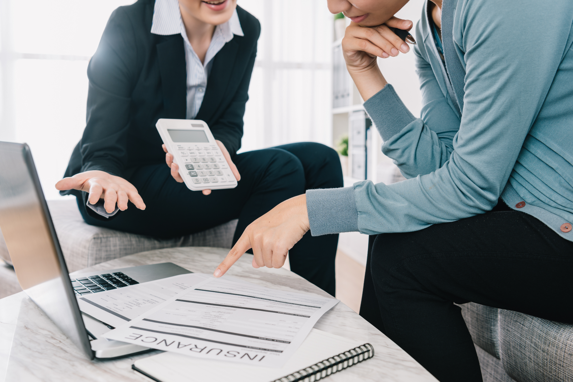 Two people reviewing insurance documents; one pointing, one holding a calculator.