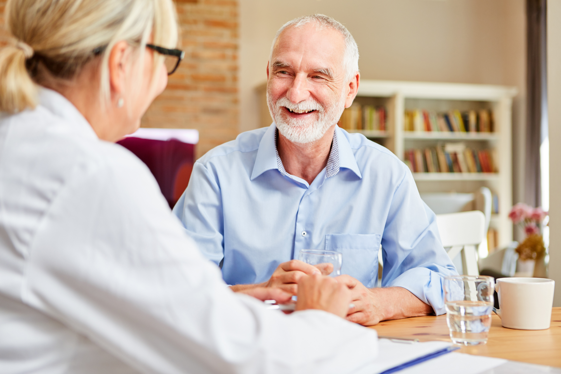 Senior man smiling at a female doctor during an appointment at a table in a home setting.