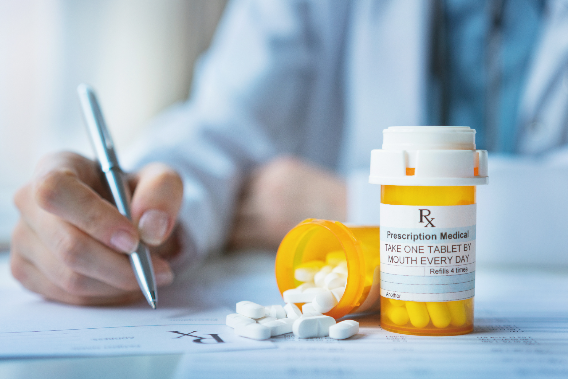 Doctor writing prescription; pills spilled from a bottle on a table.