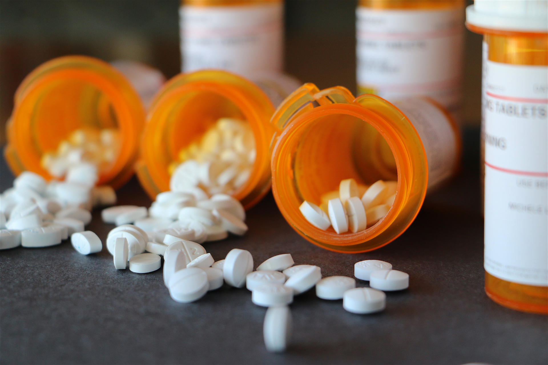 Pills spilled from orange prescription bottles on a dark surface.