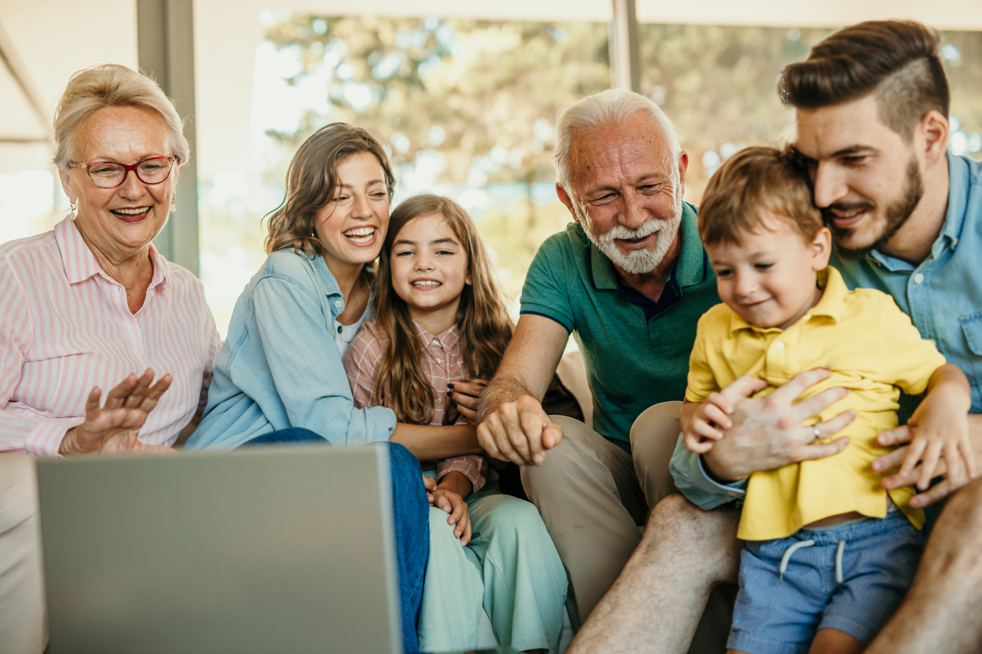 Family video call; grandparents and parents with children, smiling at a laptop.