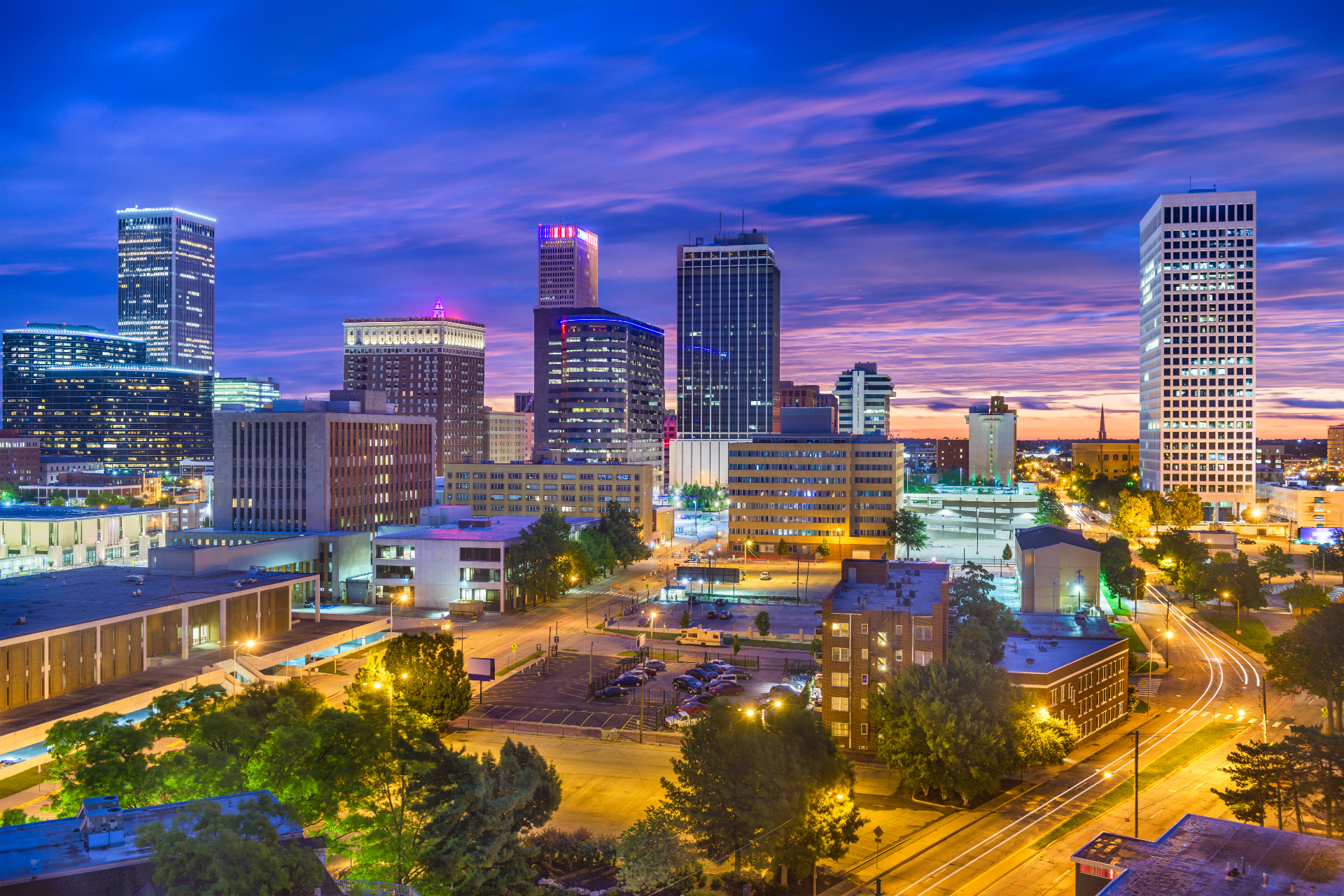 Skyline of Tulsa, Oklahoma, at dusk with lit buildings against a blue and purple sky.