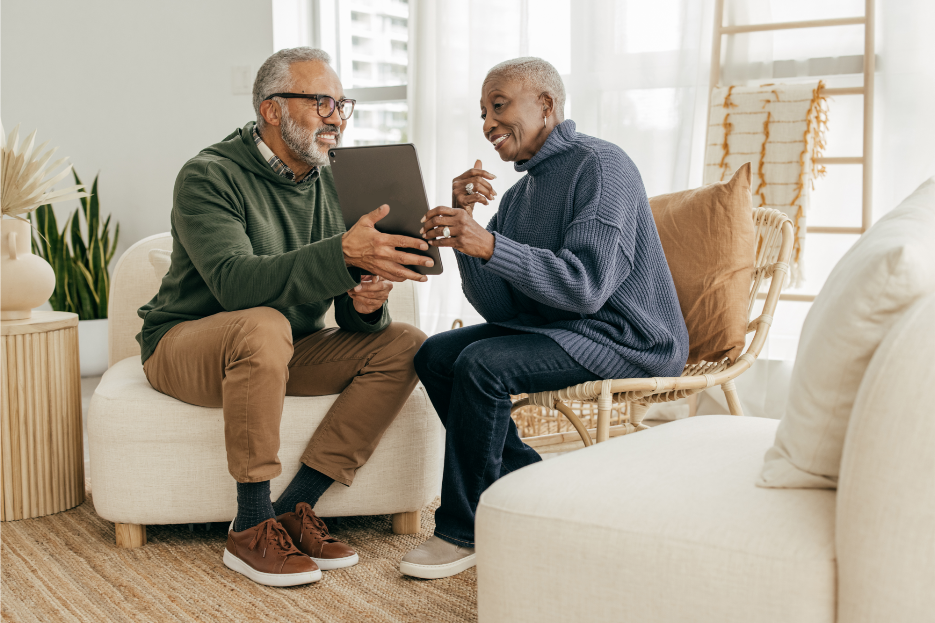 Older couple looking at a tablet, smiling. Living room setting.