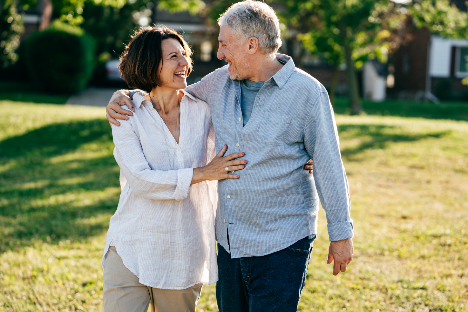 Smiling couple walks arm-in-arm in a sunny park. Woman wears white, man wears blue.