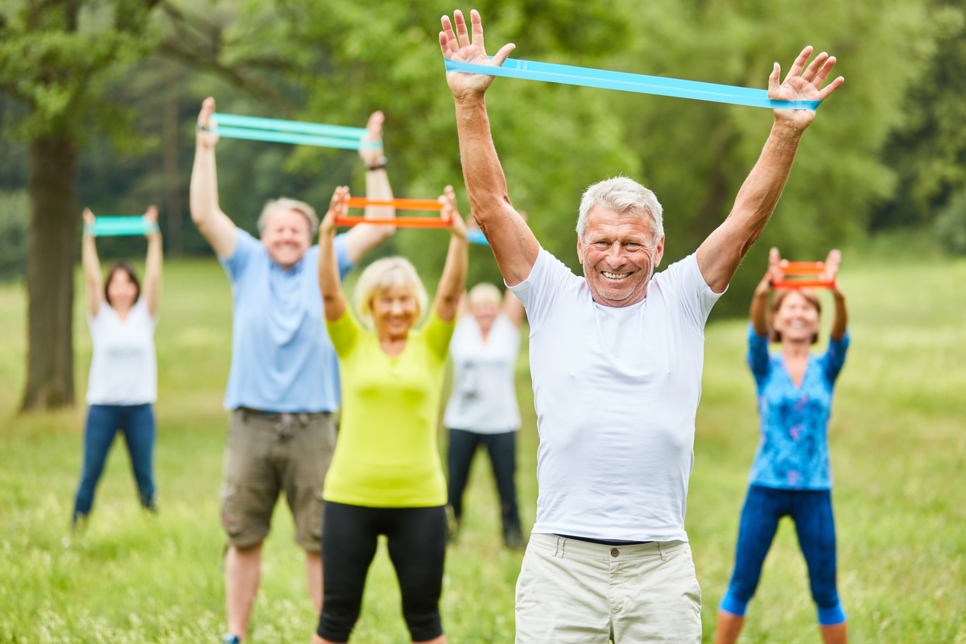 Group of seniors exercising outdoors with resistance bands, raising arms.