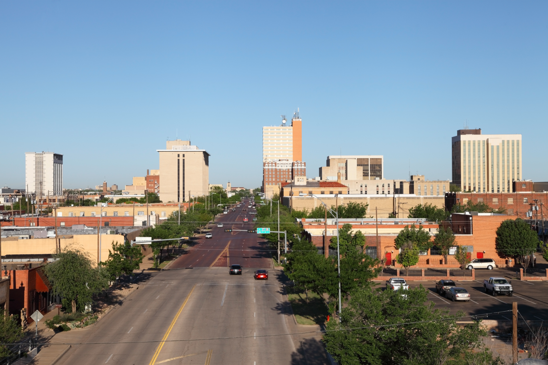 Skyline view of Lubbock, Texas, with a long road leading towards several tall buildings under a clear blue sky.