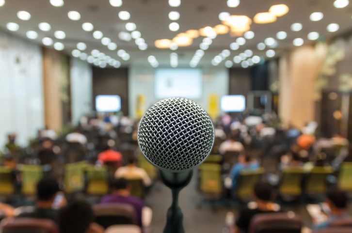 A microphone is sitting in front of a crowd of people in a conference room.