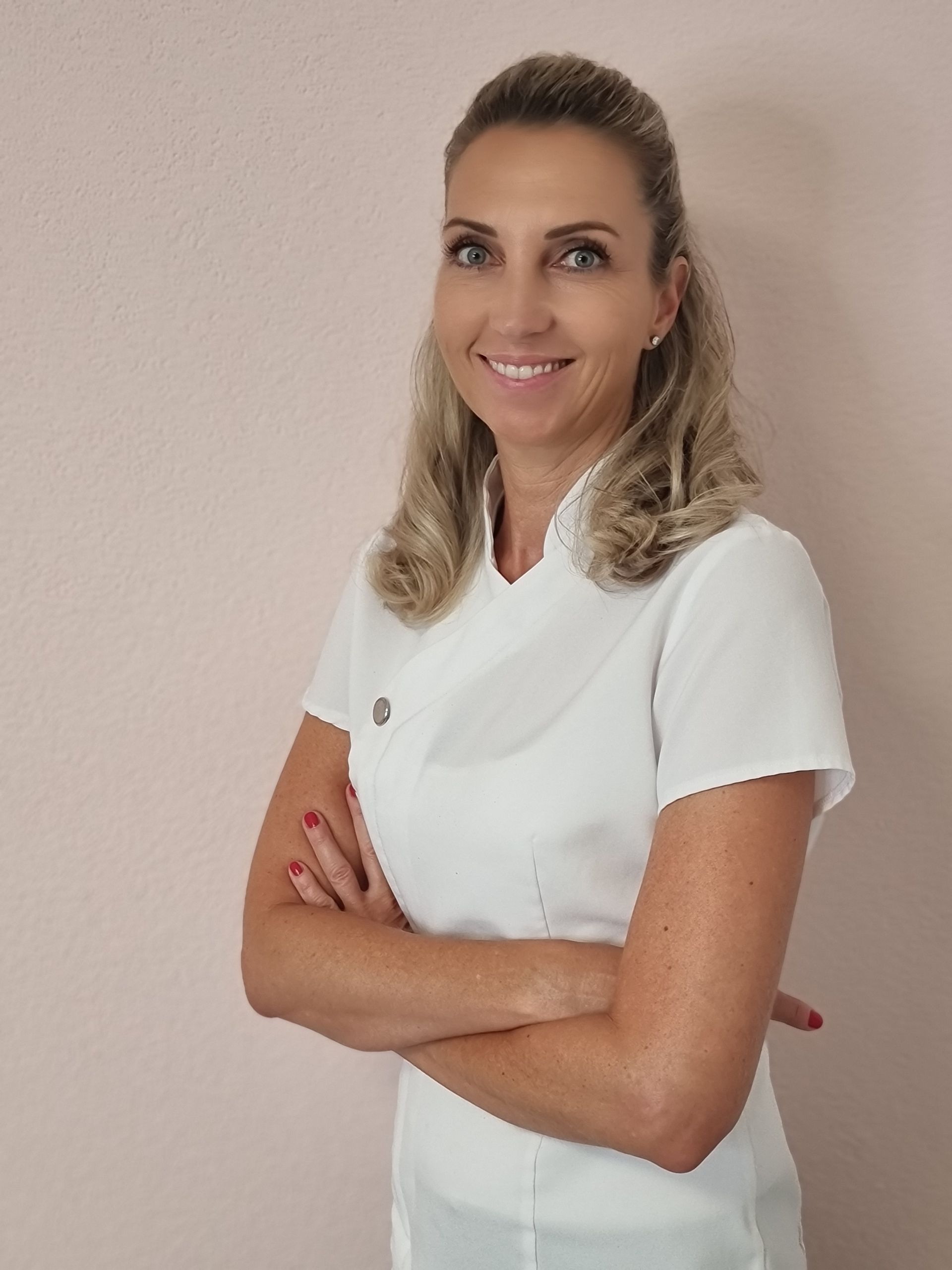 Eine Frau in einem weißen Hemd lächelt mit verschränkten Armen