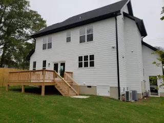 White two-story house with black roof and wooden deck on a grassy slope