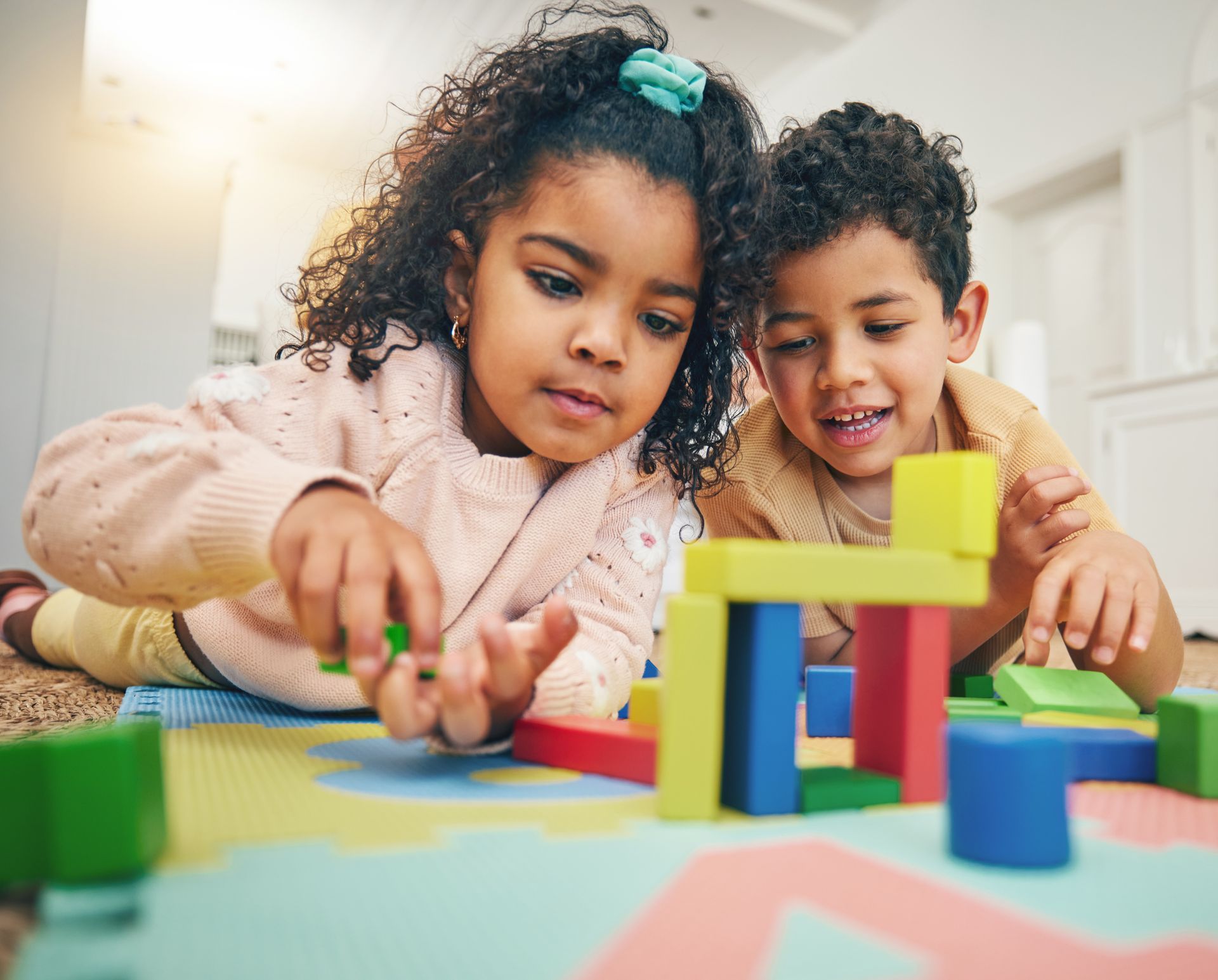A boy and a girl are playing with wooden blocks on the floor.
