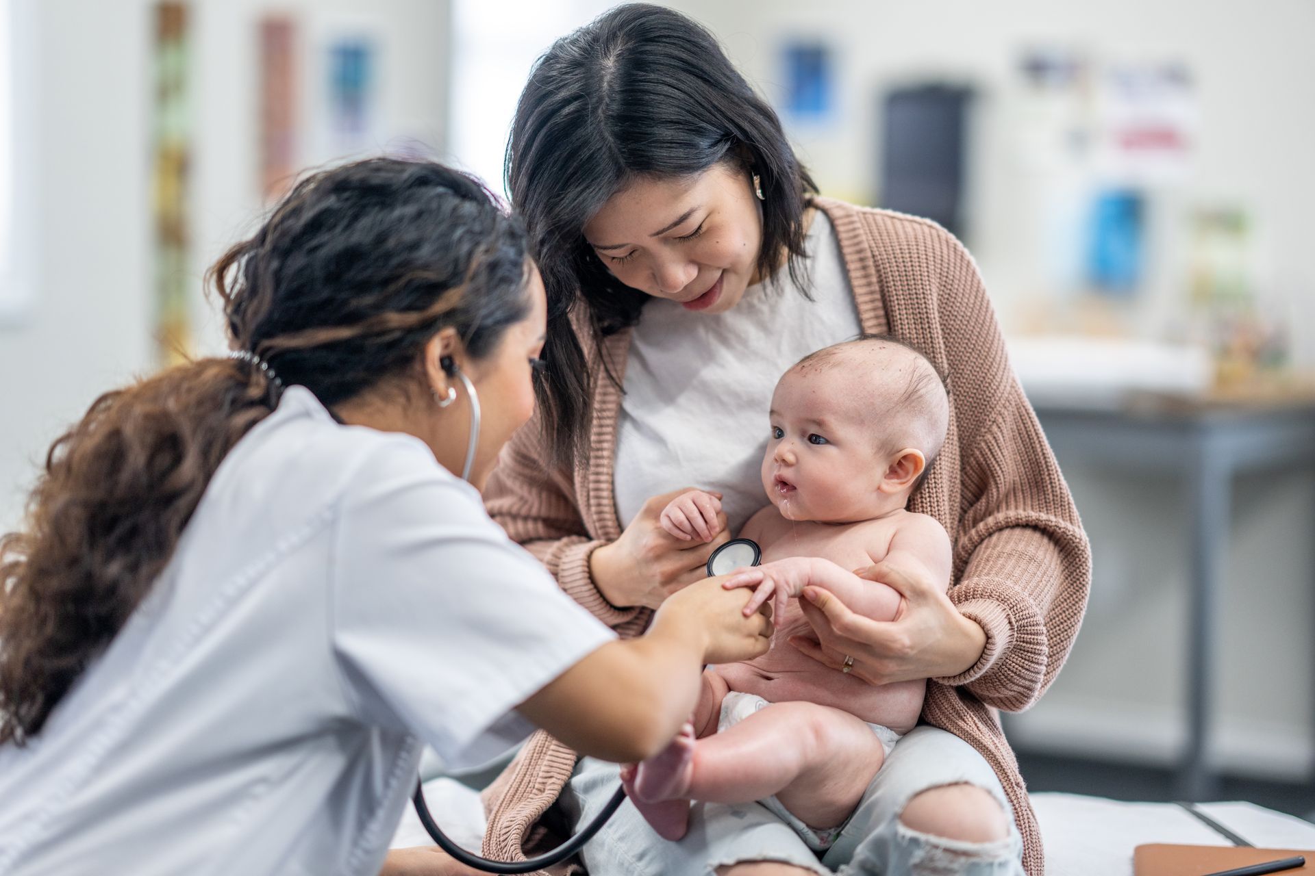 Woman holding baby and medical professional checking baby's heart with stethoscope.