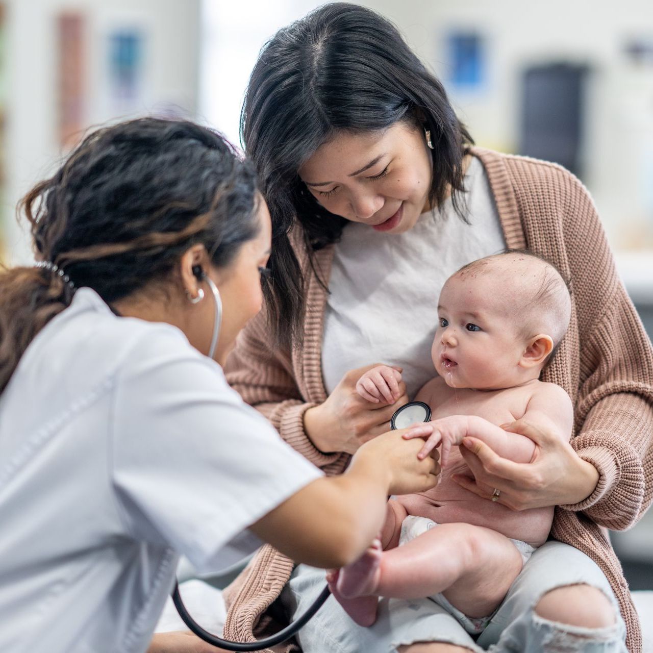 A woman is holding a baby while a doctor examines it with a stethoscope.