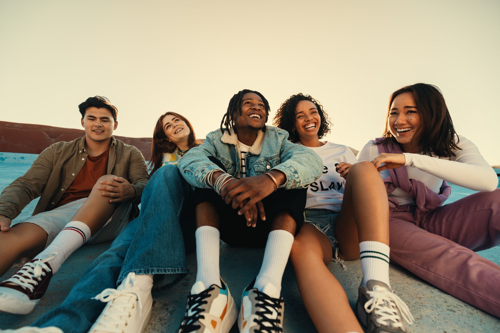 A group of young people are sitting on the ground outside.