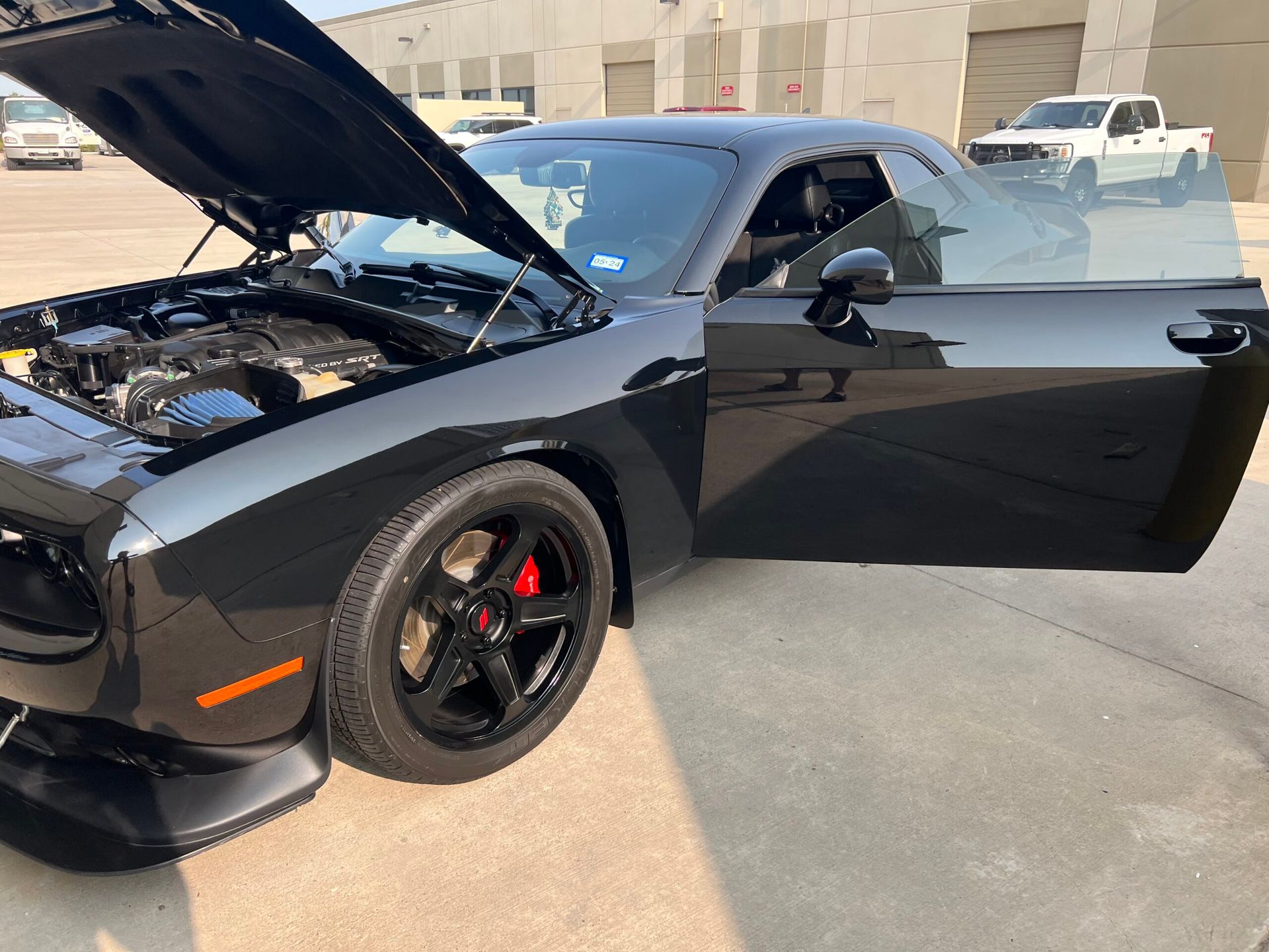 A black dodge challenger with its hood up and doors open