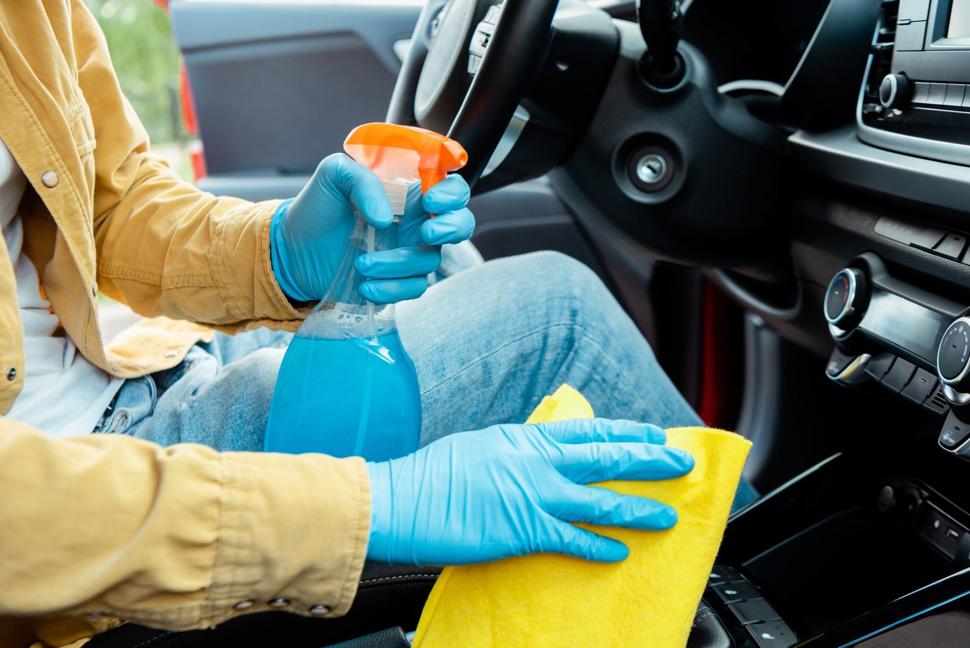 A person wearing blue gloves is cleaning the interior of a car.