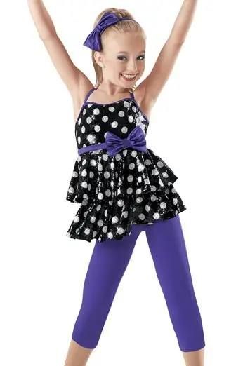 A little girl is wearing a black and white polka dot dress and purple pants