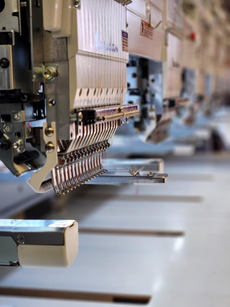 Close-up of an industrial embroidery machine with multiple needles in a factory setting.
