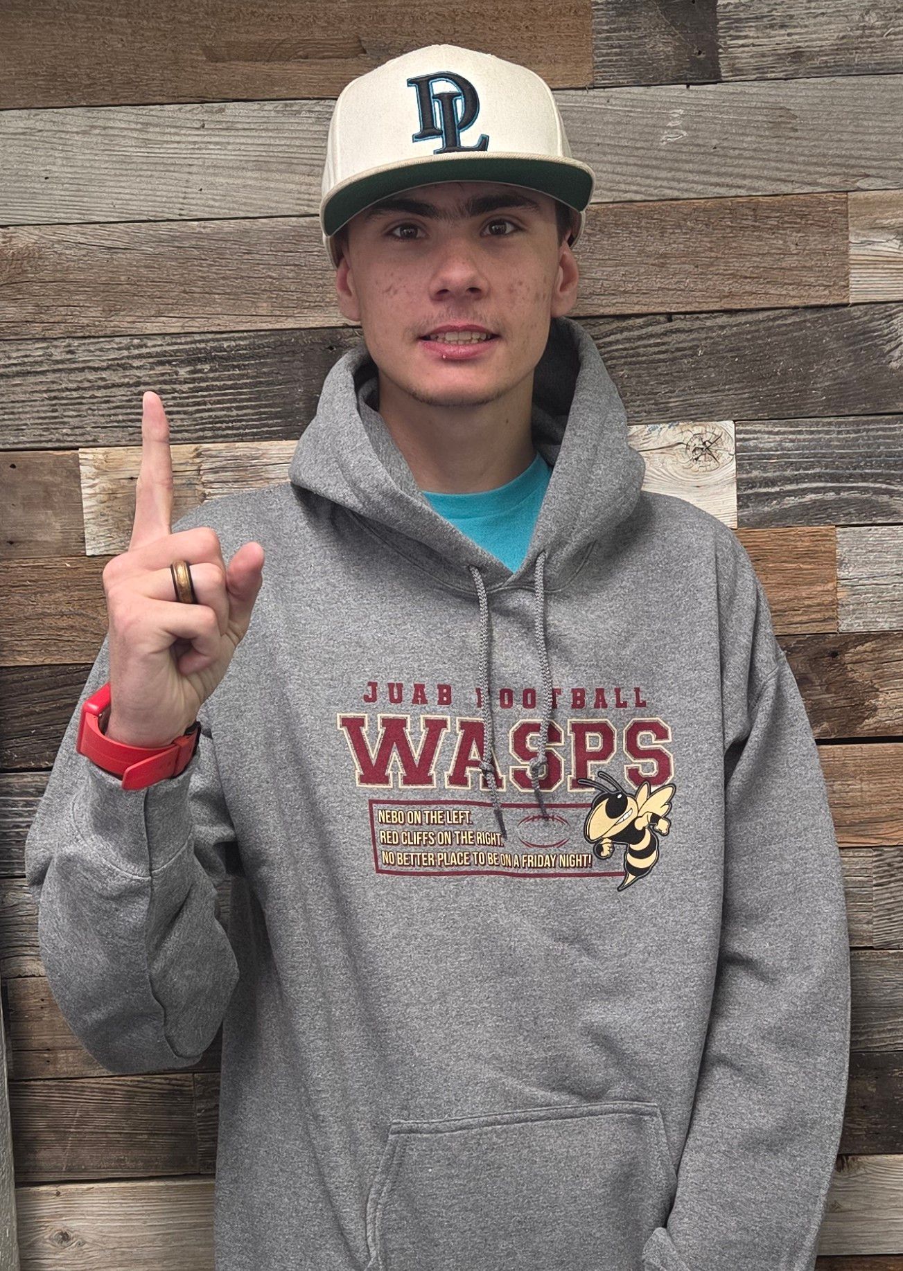 Teen in gray hoodie and cap points index finger upward. 