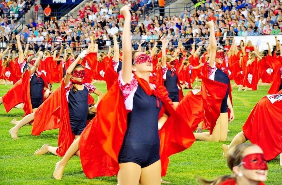 A group of people wearing red capes and masks are dancing on a field.